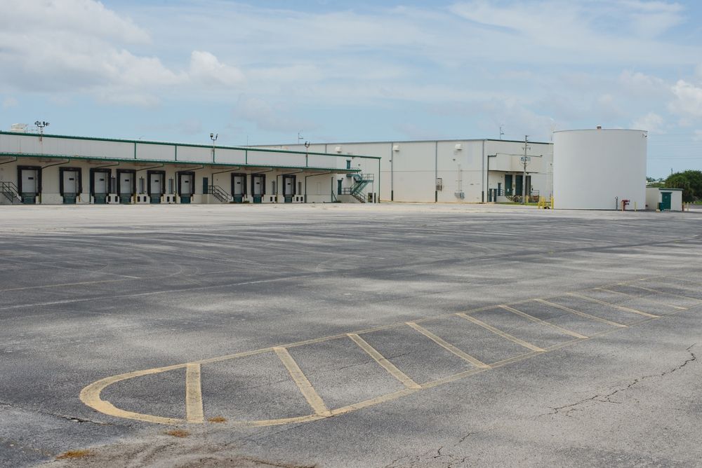 Large industrial warehouse facility with expansive asphalt truck loading and parking area, illustrating the importance of planning industrial asphalt paving projects to support heavy vehicle traffic, loading docks, and long-term pavement performance for warehouses and large commercial facilities.
